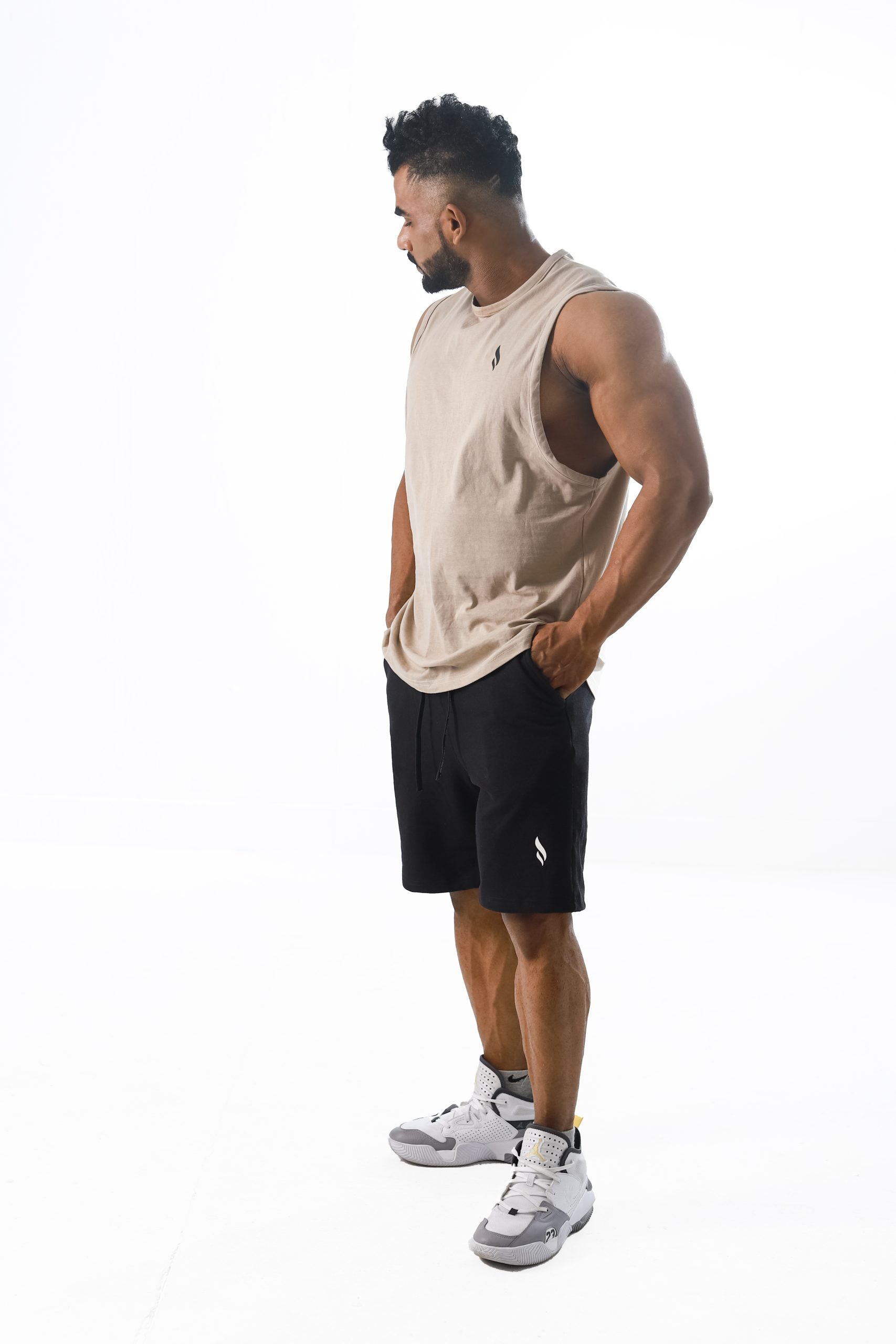 A male model wearing a Gym stereo's beige tank top and black shorts, standing against a white background.